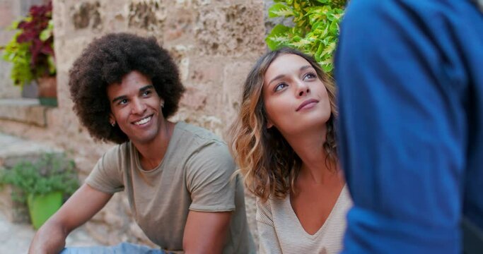Afroamerican man smiling outdoor.Three tourists talking, smiling, and having fun near a brick wall in rural town of Spello.Group of happy people talking outdoor. Friends trip in Italy.4k slow motion