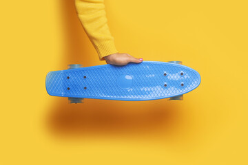 Hand holding skateboard over yellow background, youth entertainment