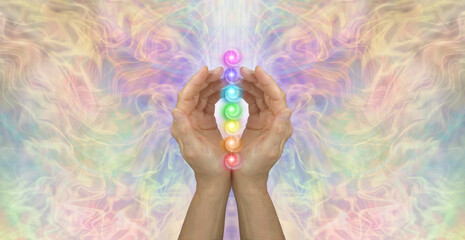 Obraz na płótnie Canvas Sacred Chakras Healing Banner Concept - Female cupped hands with seven chakra vortexes in a stack between against an ethereal multicoloured energy background with copy space 