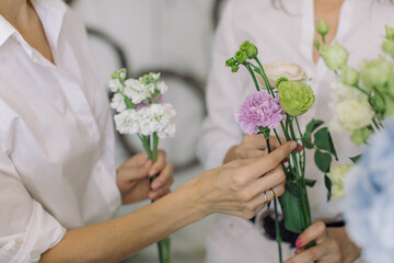 Closeup of hands of young woman florist creating bouquet of different flowers.