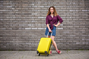 girl with a suitcase on the street. Girl with a suitcase goes on vacation. Girl with a suitcase travels. Girl with a suitcase on a wall background