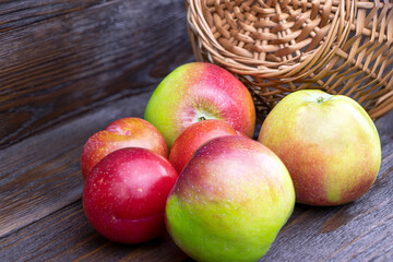 Apples and plums on a brown wooden background. Fresh fruits. Harvest. Healthy food. A wicker basket. Stick basket