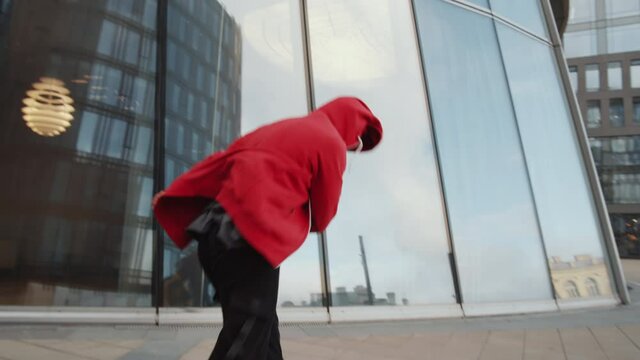 Tilt up shot of parkour man in sportswear performing side flip in front of modern glass building while training outdoors in the city