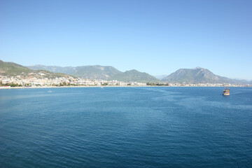 Fototapeta premium Alanya, TURKEY - August 10, 2013: Travel to Turkey. Rocks, wildlife of Turkey. Clear blue sky. The waves of the Mediterranean Sea. Water surface. Mountains and hills in the distance in the background.