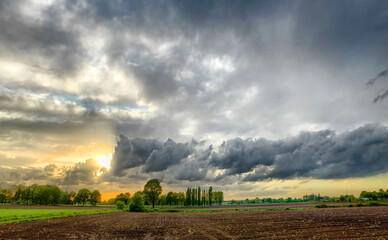 Colorful countryside sunrise or sunset over the agraric farmfields showing the dramatic colors and stormy clouds in the dark sky 