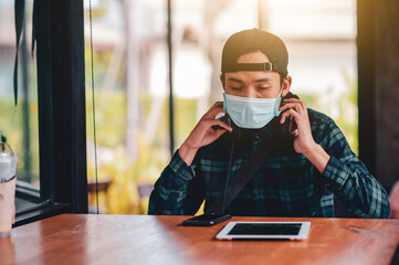 Asian man use cell phone a wearing face mask sitting cafe keep social distancing lifestyle new...