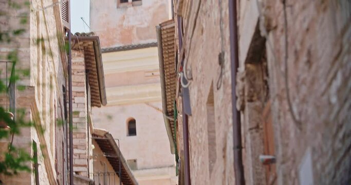 view of medieval buildings and wall in the historic town of Spello, italy. View of narrow street with bell tower on background at old italian town. Handheld tiltiing up hot