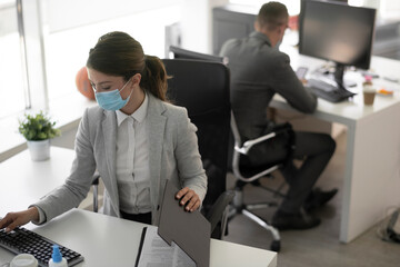 Beautiful businesswoman with medical mask working in office. Young businesswoman working on lap top.	
