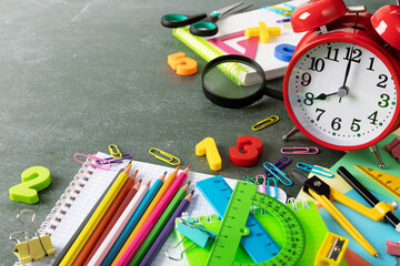 Back to school and education concept with red alarm clock and colorful school supplies on blackboard with copy space..