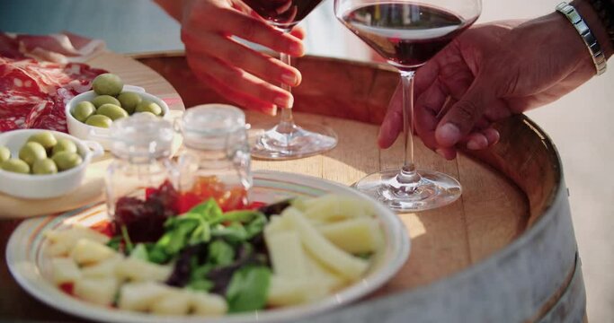 detail of man and woman hands taking wine glasses.detail of table with finger food cheese appetizer at warm sunset.Hand picking up a glass of wine. Close up shot. Friends italian trip.4k slow motion