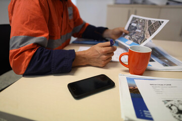Safety workplace defocused construction worker setting on a chair holding a pen while reading site...