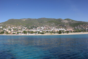 Fototapeta na wymiar Alanya, TURKEY - August 10, 2013: Travel to Turkey. The waves of the Mediterranean Sea. Water surface. Mountains and hills on the coast of Turkey. Green hills. Port.