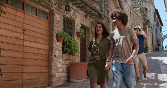 Four happy tourist walking through small street visiting rural town.Front follow. Group of multi ethnic people walking in old town.Friends vacation trip in Italy.4k slow motion