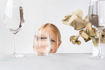 Fashion kid portrait, eye looks through the glass of water. Object distortion, optical illusion concept. Minimalistic contemporary art.