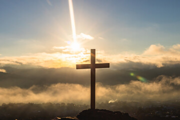 Silhouettes of crucifix symbol with bright sunbeam on top of mountain.