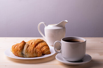 a white ceramic cup with black espresso, french croissant as breakfast or snack concept on rustic, natural texture wooden surface