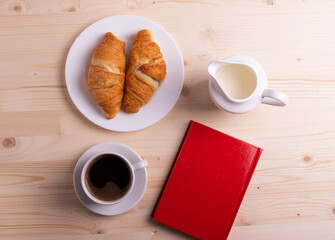 a white ceramic cup with black espresso, french croissant as breakfast or snack concept on rustic, natural texture wooden surface
