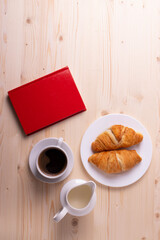a white ceramic cup with black espresso, french croissant as breakfast or snack concept on rustic, natural texture wooden surface