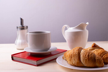 a white ceramic cup with black espresso, french croissant as breakfast or snack concept on rustic, natural texture wooden surface