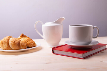 a white ceramic cup with black espresso, french croissant as breakfast or snack concept on rustic, natural texture wooden surface