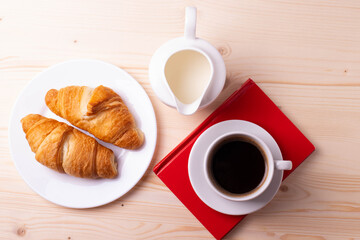 a white ceramic cup with black espresso, french croissant as breakfast or snack concept on rustic, natural texture wooden surface