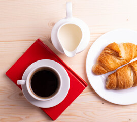 a white ceramic cup with black espresso, french croissant as breakfast or snack concept on rustic, natural texture wooden surface