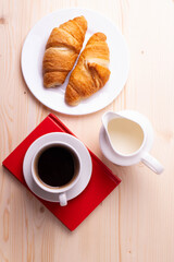 a white ceramic cup with black espresso, french croissant as breakfast or snack concept on rustic, natural texture wooden surface