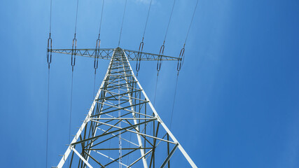 Electricity background - Voltage power lines / high voltage electric transmission tower with blue sky and shining sun