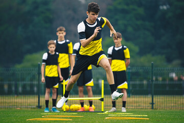Young Footballer on Training Jumping Over Obstacles. Summer Soccer Camp. Players in a Team...