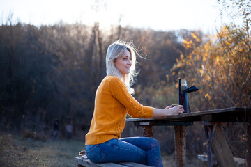 Pretty woman holding  the cup of tea in the nature. Girl sit by the table