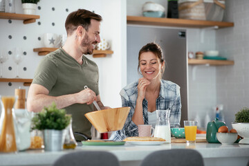 Young couple making pancakes together at home. Loving couple having fun while cooking.	
