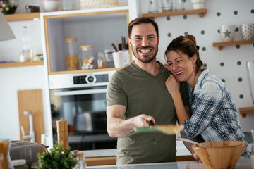 Fototapeta premium Young couple making pancakes together at home. Loving couple having fun while cooking. 