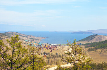 Baikal Lake. Small Sea Strait. Top view of a dirt road to a popular summer vacation spot on the shore of the warm Kurkut Bay and tourist wooden hotel houses on a hot foggy summer day