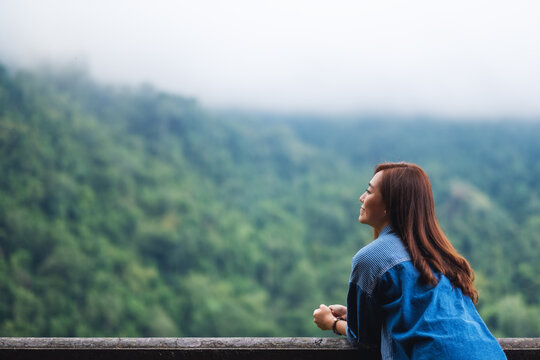Portrait image of a female traveler looking at a beautiful green mountain on foggy day