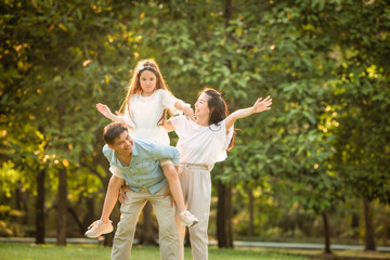 Naklejka na ściany i meble Happy family playing on the grass in the park at sunset. The concept of a happy family.