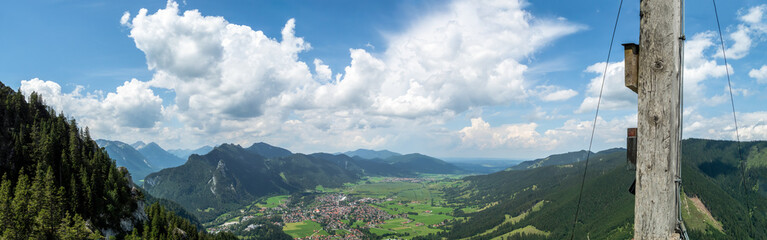 Panorama Oberammergau mit Ammergauer Bergen im Sommer bei blauem Himmel mit weißen Wolken vom Laberköpfl mit Gipfelkreuz
