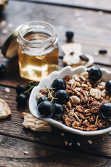 Healthy breakfast ingredients. Homemade granola, oatmeal, yogurt in the bottle, honey, berries and fruits on a wooden background. Morning aesthetics and beautiful layout on a wooden table.