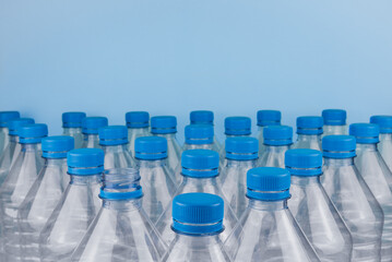 Empty clear plastic bottles with caps stacked on a blue background. Recycling and environment concept.