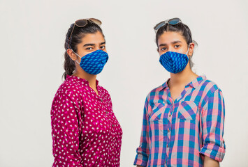 two happy girls standing with sunglass face covered with face mask and looking at camera 