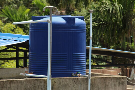 Blue plastic made water tank and pipes on top of the roof as man made water reservoir.