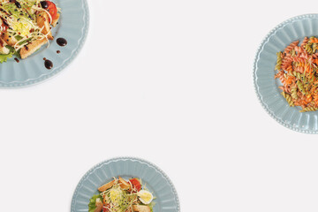 Plates with delicious food on light background with copy space. Pasta in plate. Delicious caesar salad in blue plate. 