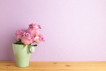 Purple rose flowers in cup on wooden table with purple background. copy space