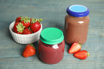 Jars with baby food and fresh strawberries on light blue wooden table