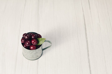 Ripe cherries in mug on gray wooden background.