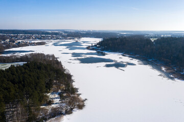 Naklejka na ściany i meble Aerial drone view flying forwards over a frozen lake with trees on the shores