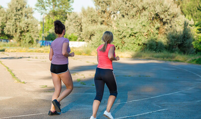 Obraz premium Young girls girlfriend are engaged in fitness, jogging outdoors in summer, sports stadium. Fitness. Physical Education.