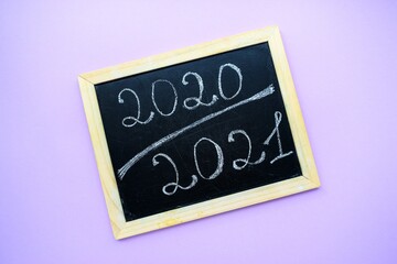 Inscription 2020 2021 on a black chalkboard chalked by hand on a purple background with a wooden frame.