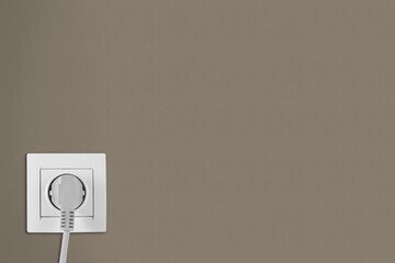 Brown wall with power socket and inserted plug, space for text. Electrical supply