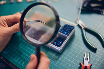 Hands of jewel maker zooming material element with a loupe
