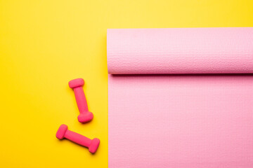 top view of pink fitness mat and dumbbells on yellow background